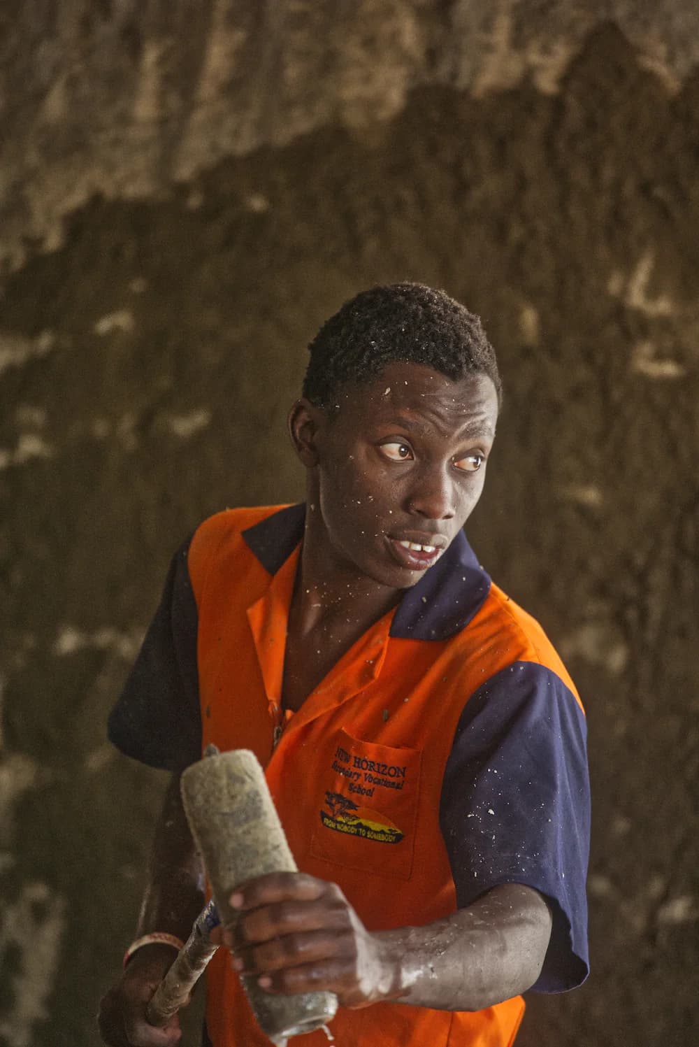 A young painter in an orange work shirt rolling paint onto a wall.